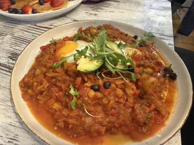 Wide plate of tomato stew with poached egg and avocado
