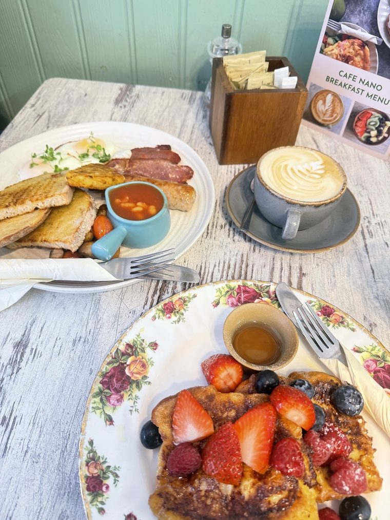 French toast with berries and syrup beside a cappuccino